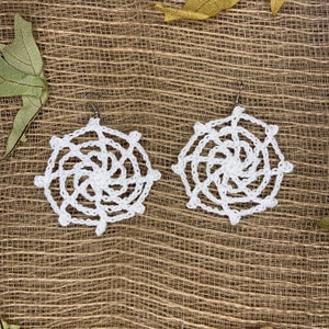 May include: A pair of white crocheted earrings with a spiral design. The earrings are hanging from silver hooks.