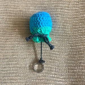 May include: A blue and green crocheted pom-pom keychain with a black cord and a silver metal ring.