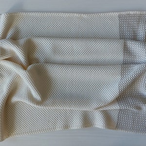 May include: A crocheted throw blanket with a cream and beige color scheme. The blanket is made with a waffle stitch and has a textured look.