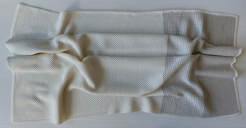 May include: A crocheted throw blanket with a cream and beige color scheme. The blanket is made with a waffle stitch and has a textured look.