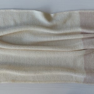May include: A white and light pink knitted throw blanket with a waffle-like texture.