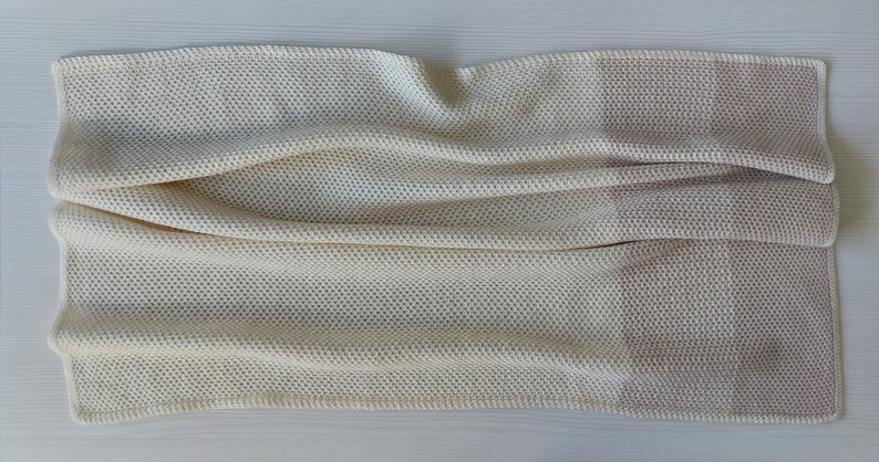 May include: A white and light pink knitted throw blanket with a waffle-like texture.