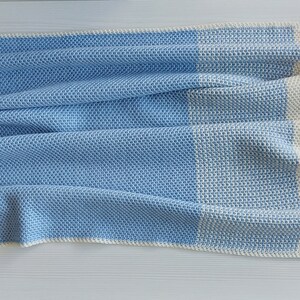 May include: A blue and white crocheted baby blanket with a textured pattern. The blanket is folded in half and has a white border.