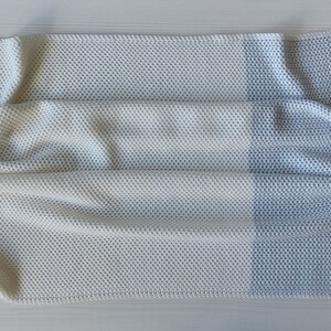 May include: A white and light blue waffle knit throw blanket with a textured pattern. The blanket is folded in half and has a soft, cozy look.