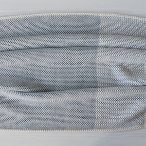 May include: A soft, gray and white knitted throw blanket with a textured pattern. The blanket is folded in half and has a white border.