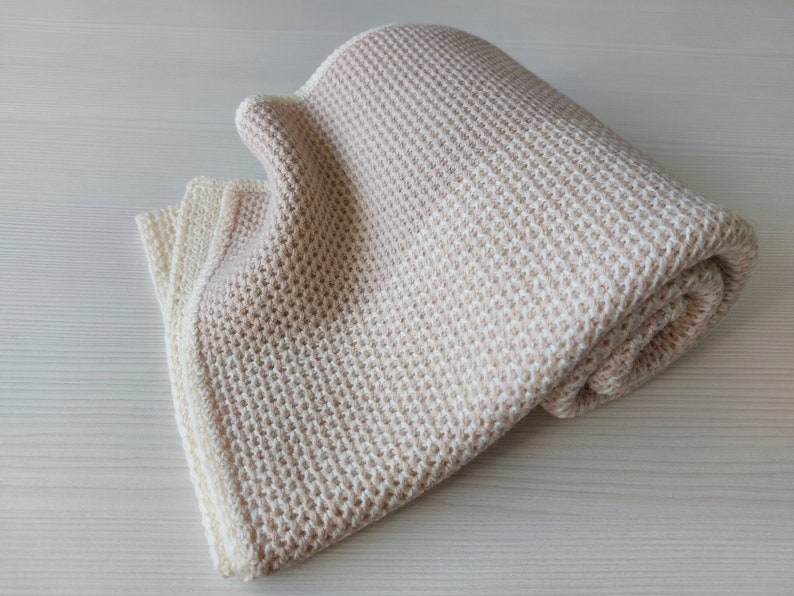 May include: A soft, beige knitted throw blanket with a waffle-like texture. The blanket is folded in half and has a white border.
