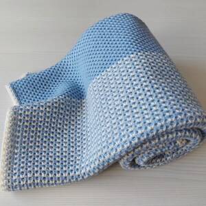 May include: A blue and white knitted baby blanket with a waffle-like texture. The blanket is rolled up and has a light blue color on one side and a white color on the other side.