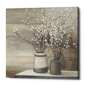 May include: Two ceramic vases with a rustic brown and white finish, filled with sprigs of white pussy willow branches against a woodgrain background.