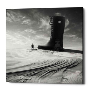 May include: A black and white photo of a giant boot with a small person walking in the distance. The boot is in a desert landscape with sand dunes.