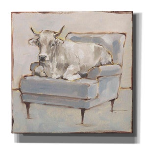 May include: A white cow sits on a light blue armchair with gold trim. The cow is looking directly at the viewer. The background is a light beige color.