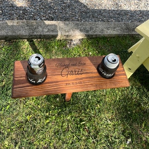 May include: Personalized wooden drink holder with two can holders and the text "Michael and Erin Garis Est. 8-3-13" engraved on the surface.