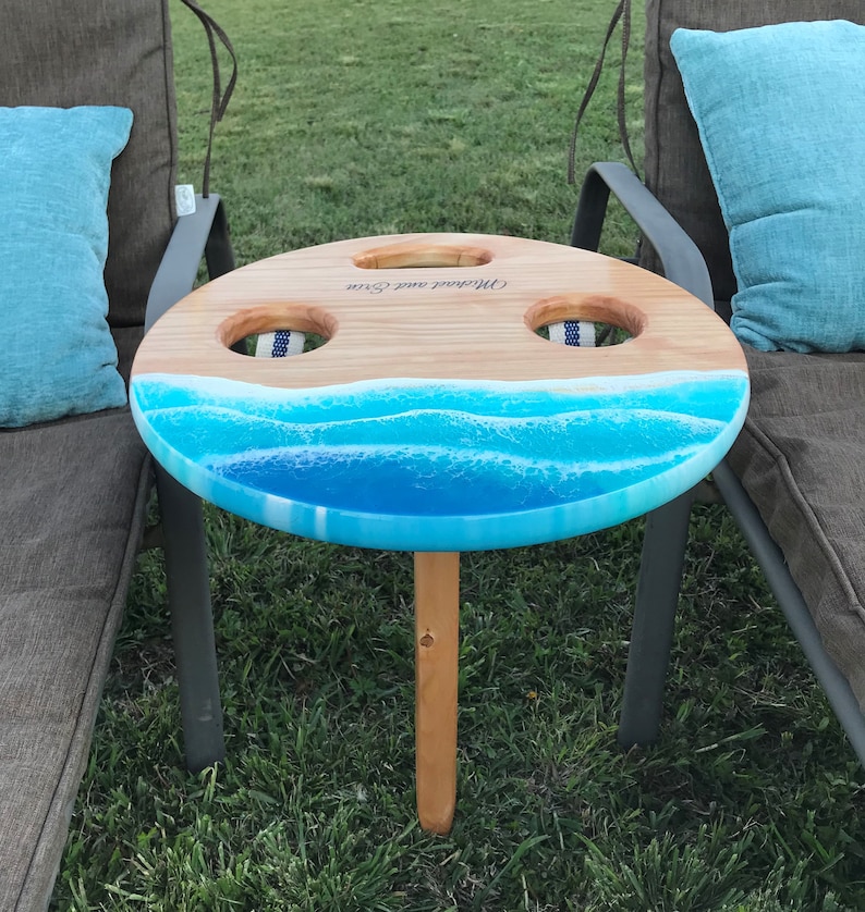 handmade sanded and stained folding portable outdoor table with 2 drink holders fitting drinks of various sizes. Available in light, medium, dark, vintage aqua stain color or light stain will add-on epoxy beach art resembling waves on the sand beach