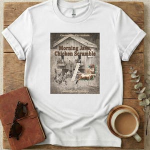May include: White t-shirt with a sepia-toned graphic depicting a chicken coop, chickens, and a relaxed animal. The text on the shirt reads "Morning Java, Chicken Scramble" and "Living My Best Feral Life."