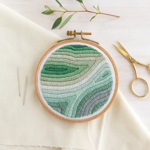 May include: A green and blue embroidered hoop art piece with a swirling, abstract design. The hoop is made of natural wood and is approximately 8 inches in diameter.