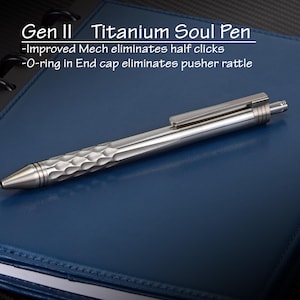 May include: A silver Titanium Soul Pen, Gen II, rests on a blue notebook. The pen features a textured grip and a clip. Text on the image reads: "Improved Mech eliminates half clicks" and "O-ring in End cap eliminates pusher rattle."