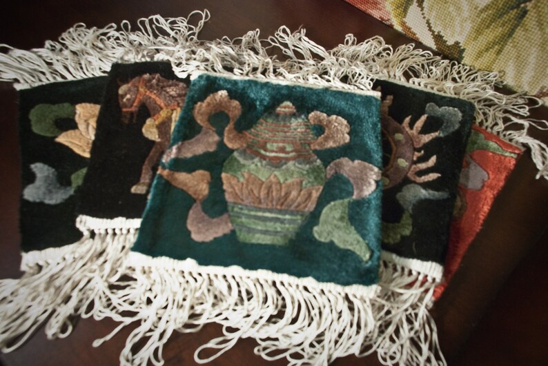 May include: Four embroidered wall hangings with fringe. The hangings feature a green background with a vase of flowers, a black background with a horse, a black background with a floral design, and a red background with a floral design.