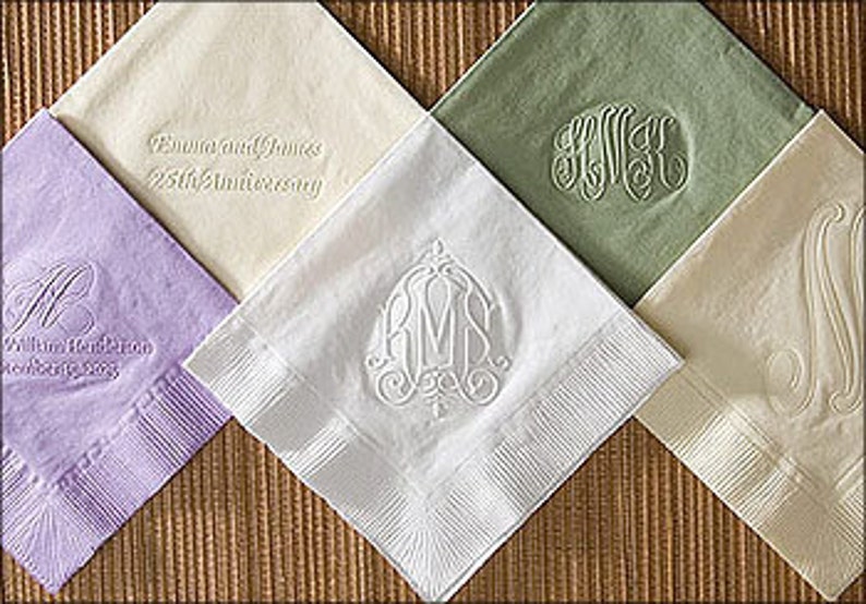 以下が含まれることがあります： 白の刺繍が施された、5色の異なるリネンナプキン。ナプキンには、モノグラム、花柄、25周年記念のメッセージなど、さまざまなデザインが施されています。