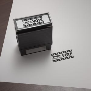 May include: A black rectangular stamp with the words "THINK VOTE BEFORE YOU" printed in white. The stamp is on a white surface, with a stamped impression of the same text nearby.