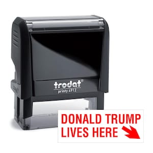 May include: A black Trodat printy 4912 stamp with the text "DONALD TRUMP LIVES HERE" in red, with a red arrow pointing right. The stamp is on a white background.