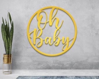 Może przedstawiać: Okrągły, złoty drewniany znak z napisem "Oh Baby" napisanym kursywą.