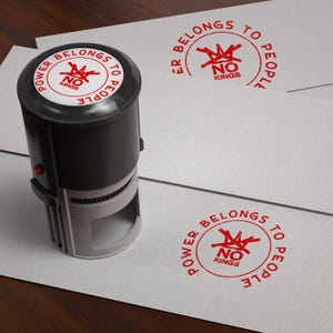 Puede incluir: Un sello autoentintable negro y plateado con el texto "POWER BELONGS TO PEOPLE" que rodea un gráfico rojo y las palabras "NO KINGS". El sello está junto a varias impresiones del mismo diseño en papel blanco.
