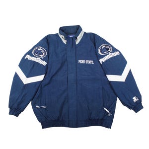 Puede incluir: Chaqueta azul marino de Penn State con detalles blancos. La chaqueta presenta el logotipo de Penn State en las mangas y el texto "PENN STATE" en el pecho. Tiene cuello alto y cierre de cremallera.