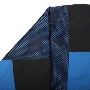 May include: Close-up of a section of a garment with a patchwork design. The design features black, blue, and a mesh fabric with blue polka dots. The fabric appears to be a lightweight material.