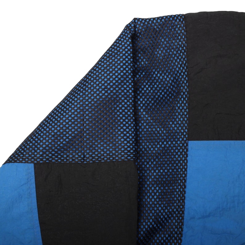May include: Close-up of a section of a garment with a patchwork design. The design features black, blue, and a mesh fabric with blue polka dots. The fabric appears to be a lightweight material.