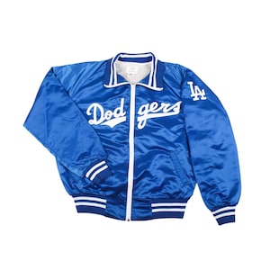 Può includere: Giacca in raso blu reale con dettagli bianchi e cerniera completa. La giacca presenta la scritta "Dodgers" in bianco sul petto e il logo della squadra sulla manica. Il colletto e i polsini hanno strisce bianche.