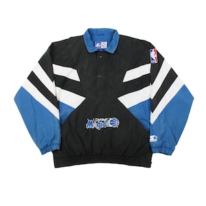 Op de afbeelding: Zwarte, blauwe en witte vintage Orlando Magic NBA Starter pulloverjas. Voorzien van het teamlogo, NBA-logo en Starter-logo. De jas heeft een blauwe kraag en mouwen, met witte en zwarte accenten.