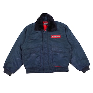 May include: A dark navy blue bomber jacket featuring a black faux fur collar, a red interior lining, and a rectangular red patch on the chest with the white text Bridgestone. The jacket includes two large front pockets and ribbed cuffs.