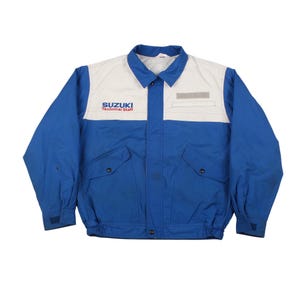 Peut inclure: Veste bleue et blanche Suzuki Technical Staff. La veste a un col, deux poches avant et une fermeture boutonnée. Le logo Suzuki est imprimé sur la poitrine.