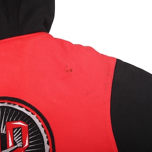 Pu&ograve; includere: Felpa con cappuccio rossa e nera. La felpa ha un corpo rosso e maniche e cappuccio neri. Una grande grafica &egrave; visibile in basso a sinistra, con elementi bianchi, grigi e neri. Il design &egrave; stilizzato.