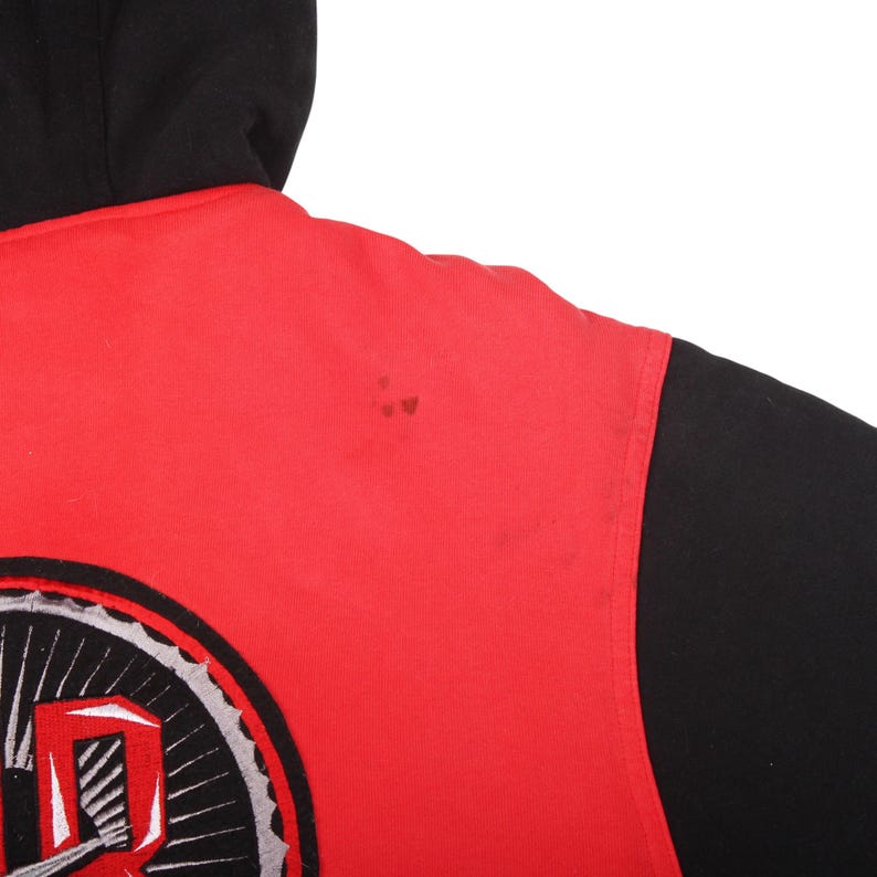 Pu&ograve; includere: Felpa con cappuccio rossa e nera. La felpa ha un corpo rosso e maniche e cappuccio neri. Una grande grafica &egrave; visibile in basso a sinistra, con elementi bianchi, grigi e neri. Il design &egrave; stilizzato.