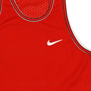 May include: Red basketball jersey with a white Nike swoosh logo. The jersey is made of a mesh material and has a black and white trim around the neck.