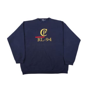May include: Navy blue sweatshirt with the text "CP RL-94" in yellow and red. The sweatshirt has a crew neck and long sleeves. The letters "CP" are in a stylized font.