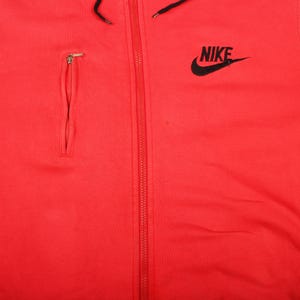 Pu&ograve; includere: Felpa con cappuccio rossa brillante con logo Nike nero sulla parte superiore destra del petto. La felpa con cappuccio presenta un cordoncino nero, una tasca con cerniera sul petto sinistro e una cerniera a tutta lunghezza sul davanti.