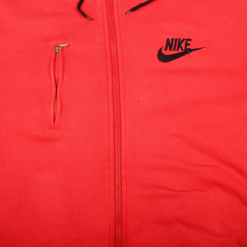 Pu&ograve; includere: Felpa con cappuccio rossa brillante con logo Nike nero sulla parte superiore destra del petto. La felpa con cappuccio presenta un cordoncino nero, una tasca con cerniera sul petto sinistro e una cerniera a tutta lunghezza sul davanti.