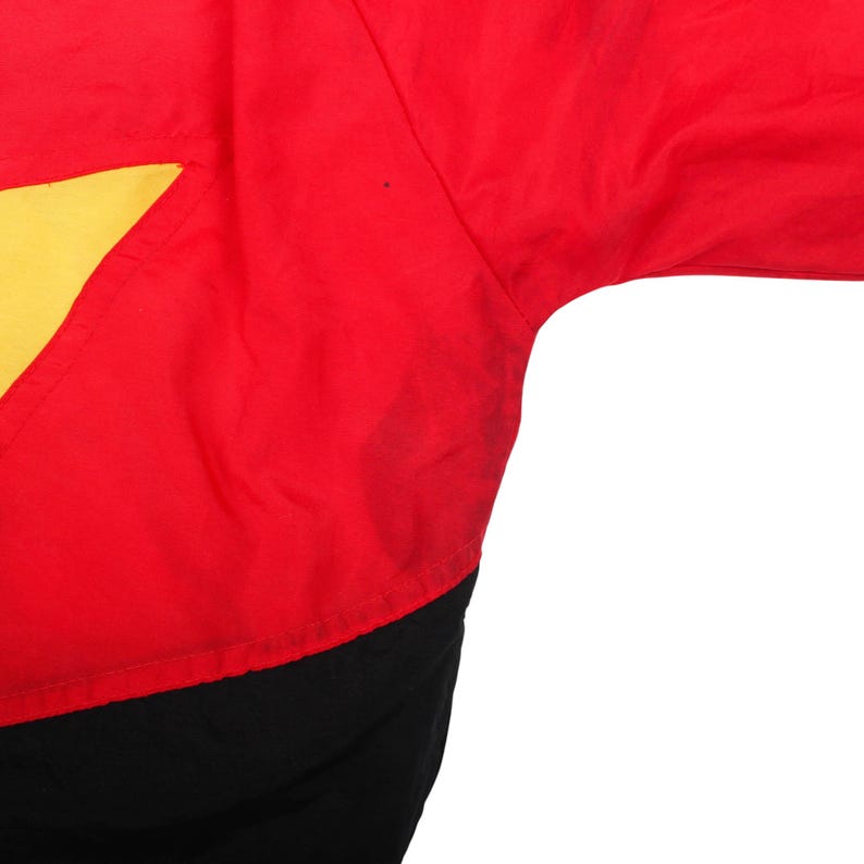 May include: A bright red jacket featuring a large yellow star graphic on the left side. The garment is constructed with a solid black panel along the bottom hem and includes long sleeves with a smooth, lightweight fabric texture throughout the piece.