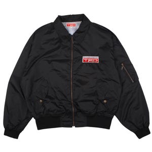 May include: A black zip-up bomber jacket featuring a fold-down collar, ribbed cuffs and hem, and two front pockets with snap closures. A rectangular patch on the left chest displays the white text Racing Development and the red TRD logo.
