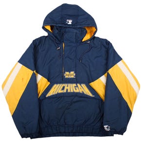 May include: A navy blue pullover jacket with a hood, featuring yellow and white color-blocked sleeves. The front displays the word MICHIGAN in yellow lettering, a small Michigan logo on the chest, and a Starter logo on the hood and sleeve cuff.