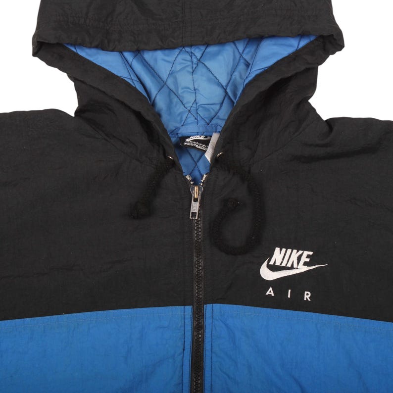 May include: Black, blue, and white Nike Air hooded jacket. The jacket has a black hood and upper body, a blue lower body, and a blue quilted lining. The Nike logo and "AIR" are printed in white on the chest. The jacket has a full zipper.