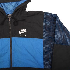 May include: A black, blue, and white Nike Air jacket with a hood. The jacket features a blue lower panel, black upper panel, and a blue mesh design on the right sleeve. The Nike logo is prominently displayed on the chest.