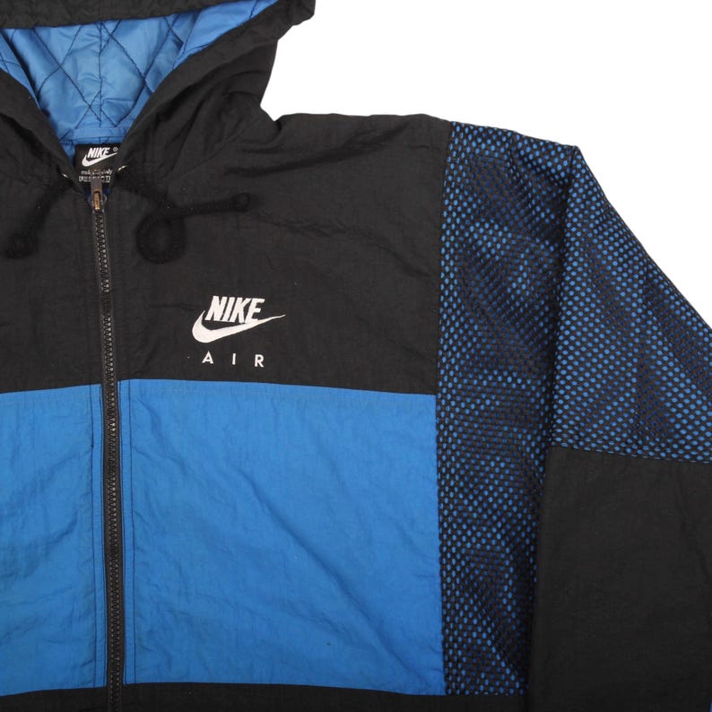 May include: A black, blue, and white Nike Air jacket with a hood. The jacket features a blue lower panel, black upper panel, and a blue mesh design on the right sleeve. The Nike logo is prominently displayed on the chest.