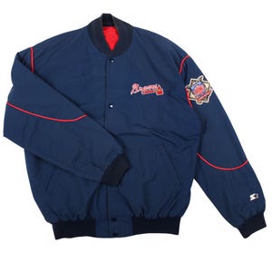 Op de afbeelding: Een marineblauw Starter-jack met een rood-wit Braves-logo geborduurd op de borst. Het jack heeft een drukknoopsluiting, geribbelde boorden en zoom, rode biezen en een herdenkingsbadge op de linkermouw.