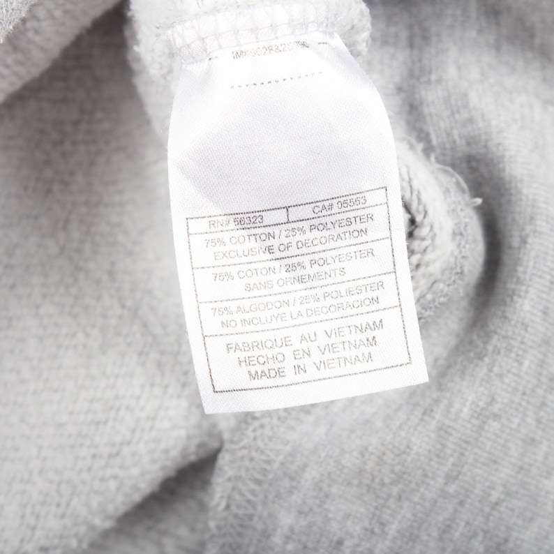 May include: A close-up shot of grey fabric with a white label attached. The label shows text including "75% COTTON/25% POLYESTER" and "MADE IN VIETNAM". The fabric is likely part of a piece of clothing.