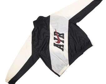 May include: Black, white, and gray Nike Air jacket. The jacket has a white vertical stripe down the center with the word "AIR" in black block letters and a red Nike swoosh. The sleeves are white with black trim.