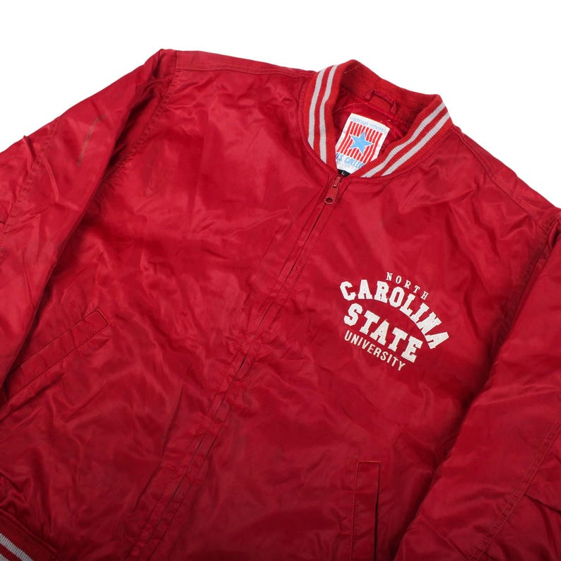 retro university graphic basic apparel, iconic wolfpack country vintage piece, faded red stadium gameday outfit , vintage nc state, north carolina state, 90s college, varsity jacket, bomber coat, windbreaker jacket, red sports outerwear, athletic wear, blockcore clothes, wolfpack merchandise, retro team gear, varsity clothing, prep style outfit, ivy league fashion, americana vintage, old school streetwear, oversized jacket, boxy fit pullover, autumn winter layering, school spirit top,