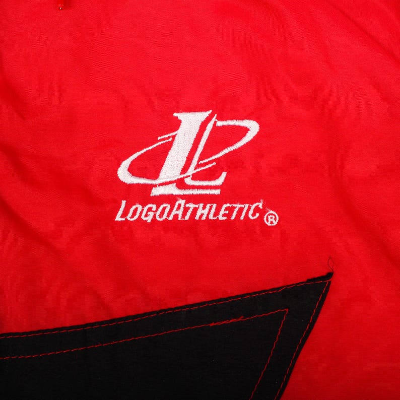 May include: A bright red fabric garment featuring a white embroidered logo of a stylized letter L enclosed in an oval shape, with the text LogoAthletic positioned directly below the emblem. A black triangular panel is visible at the bottom edge.
