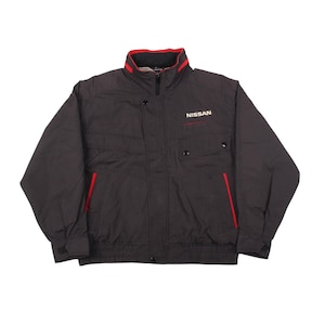 May include: A dark grey jacket with red detailing, a high collar, and a zip fastening. The jacket has two front pockets and the word "NISSAN" printed on the chest. Red piping is visible on the pockets and collar of the jacket.